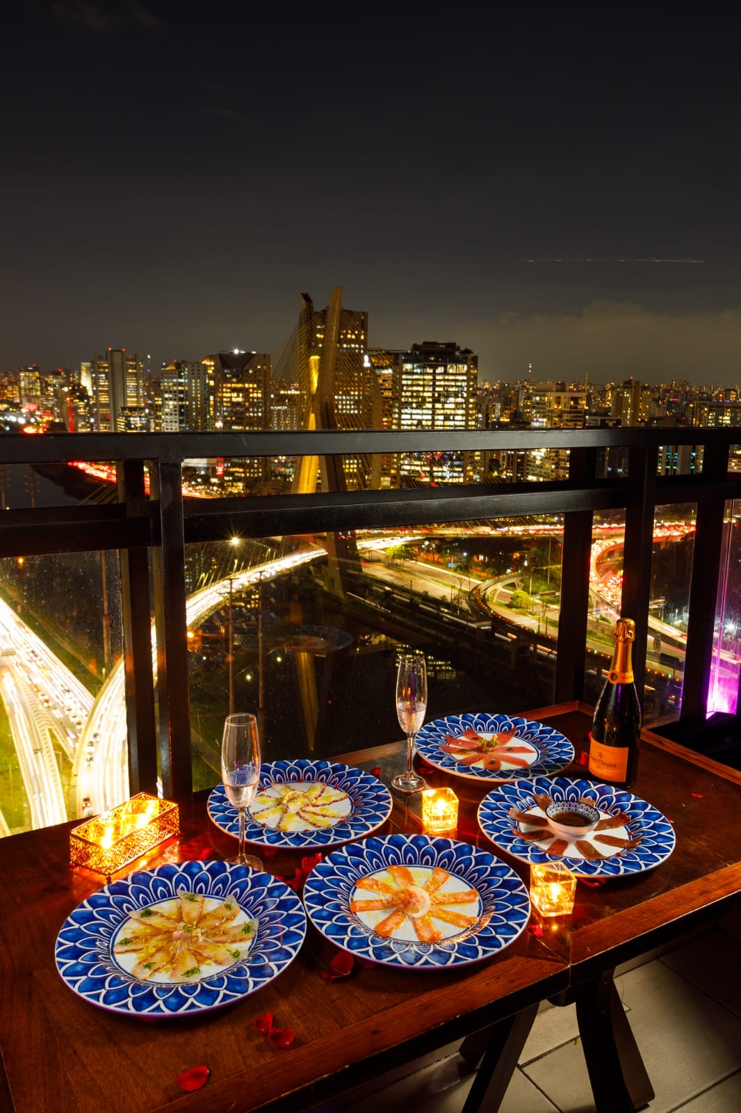 Mesa posta na varanda do Terrazza Rooftop à noite, com champanhe e vista da ponte estaiada