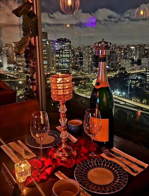 Taças, espumante e velas em mesa romântica com a cidade ao fundo